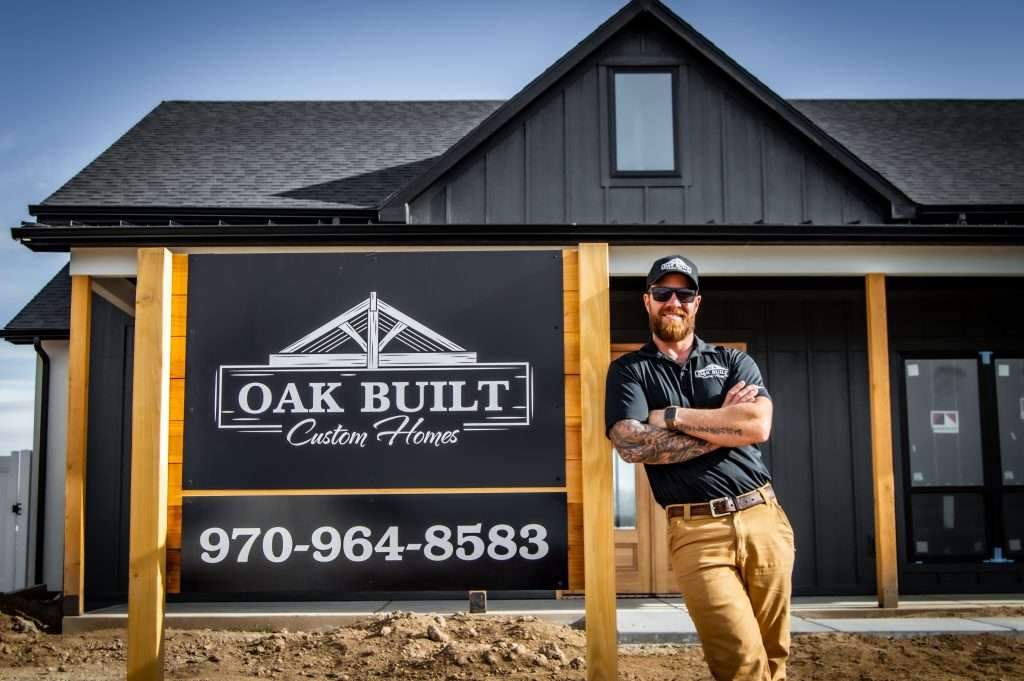 Oak Built Homes Charlie Mezzenga standing next to a sign with their logo and phone number.