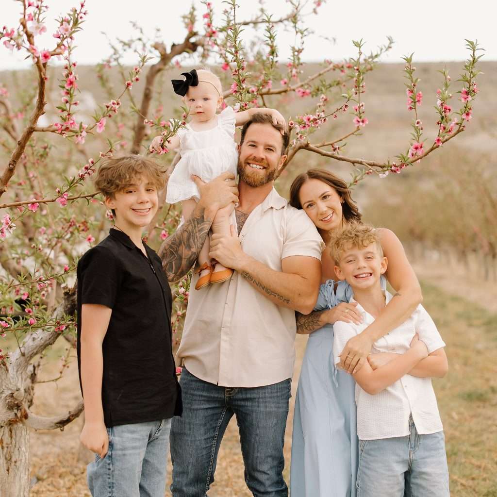 Charlie Mezzenga and Wife Courtney with their family of 5 standing in a peach orchard in Western Colorado.